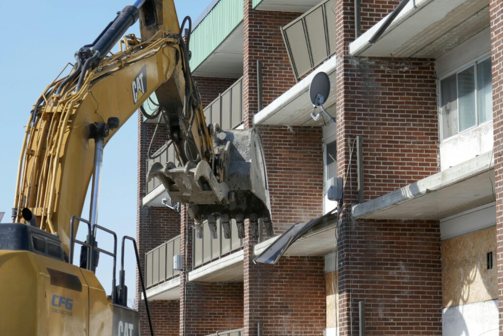 Excavator demolishing a brick residential building in an urban area.